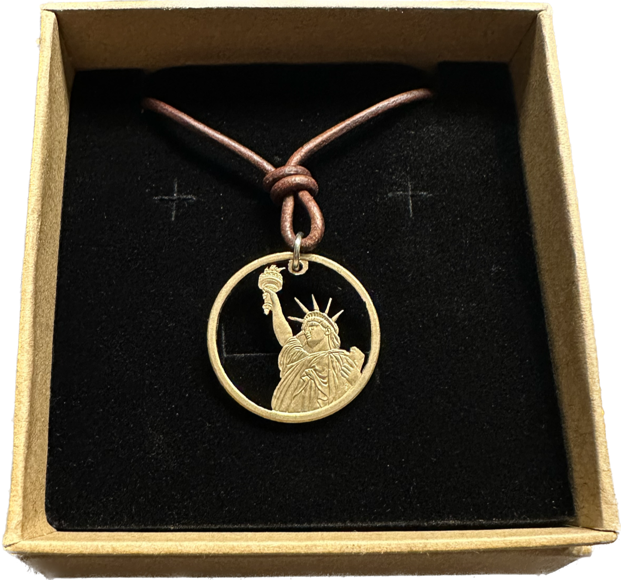 U.S. Statue of Liberty Gold Dollar Hand Cut Coin Necklace with leather cord in a brown kraft box on a black velvet background.