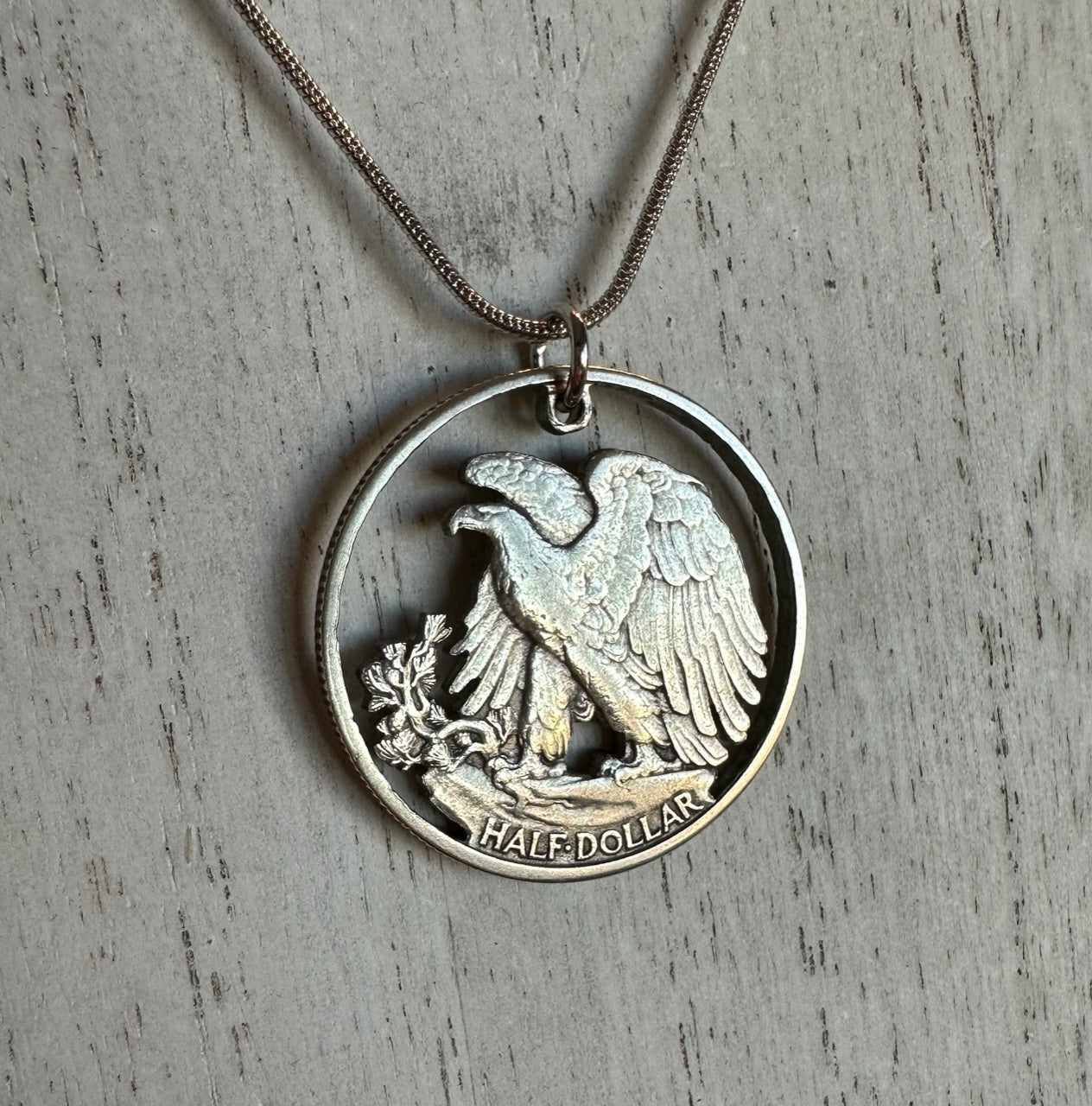 U.S. Walking Liberty Silver Hand Cut Coin Necklace (Eagle) with a snake chain on a white wood background.