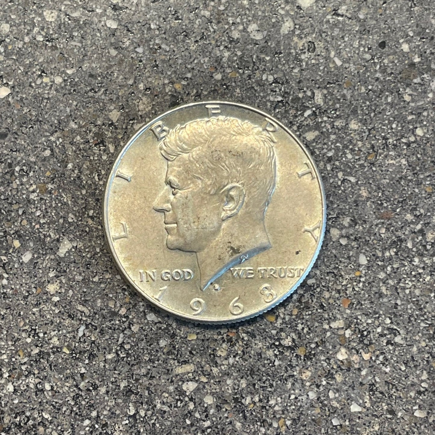 JFK Silver Half Dollar Coin (front) on a concrete background.