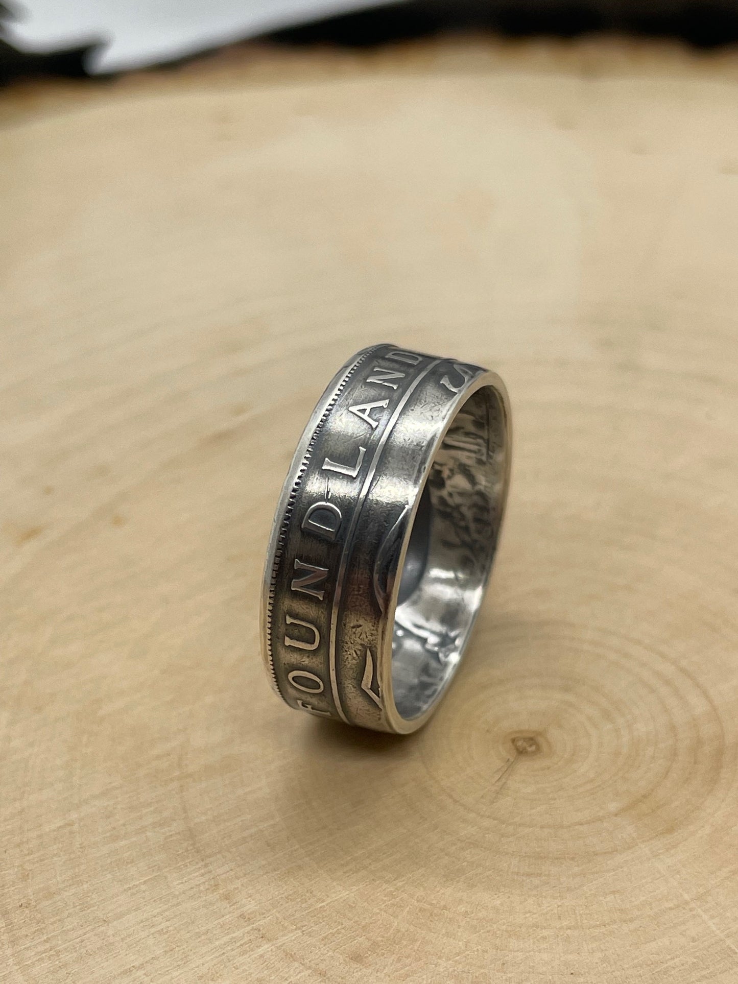 Newfoundland 50 Cents Silver Coin Ring on its edge on a light wood round.