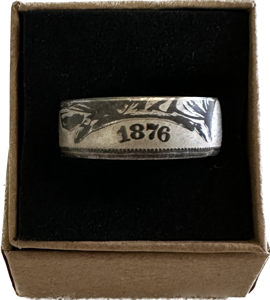 Seated Liberty Silver Half Dollar Coin Ring (reverse patina) in a brown kraft box on a black velvet background.