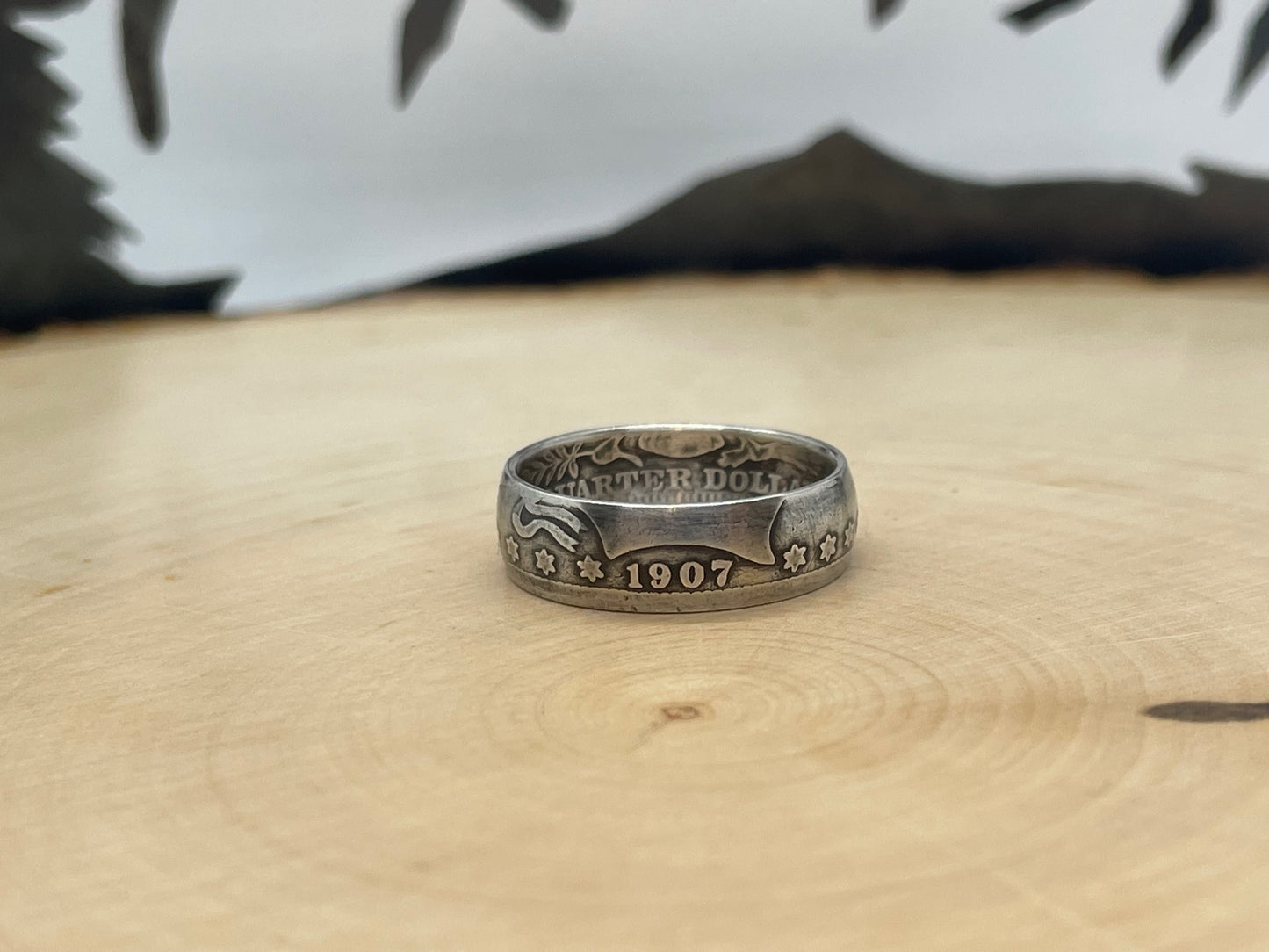 Barber Silver Quarter Coin Ring (front) on a light wood round with mountain outline in the background. - Mountainstruck Coin Jewelry