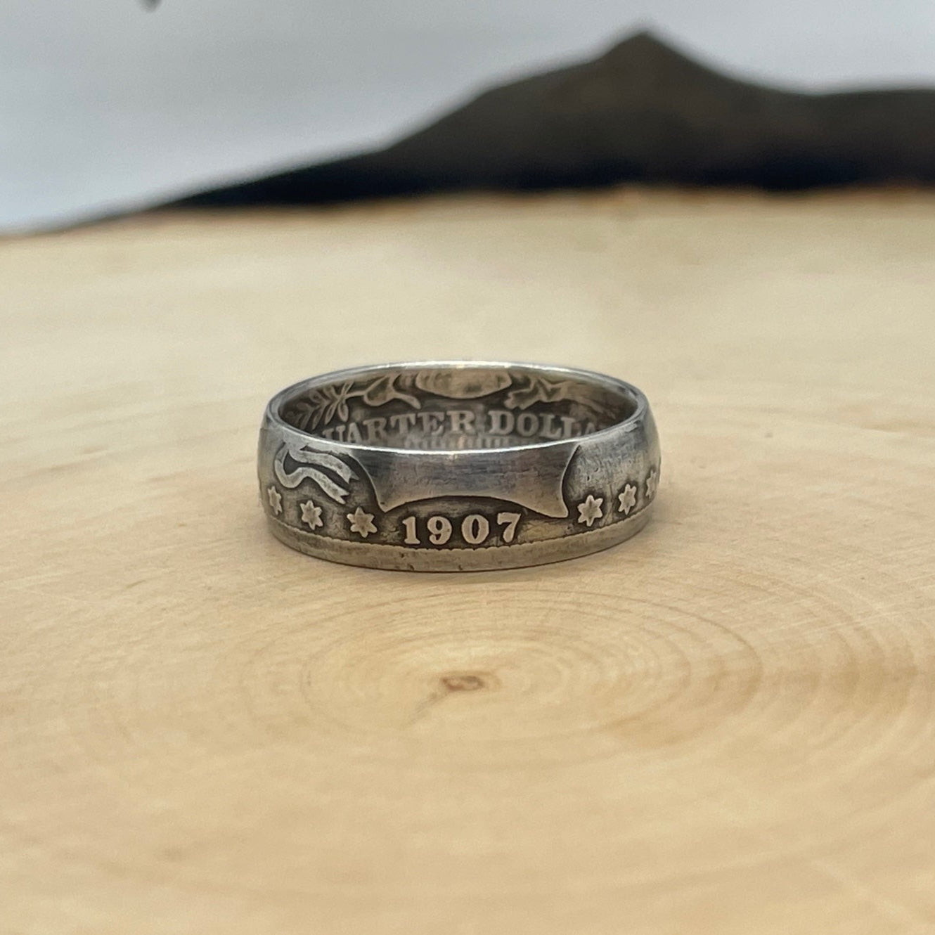 Barber Silver Quarter Coin Ring (front) on a light wood round with mountain outline in the background. - Mountainstruck Coin Jewelry