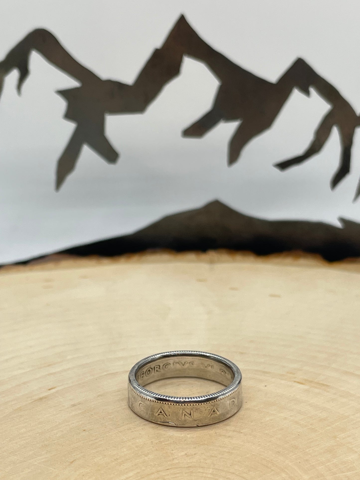 Canada 25 Cents Silver Coin Ring on a light wood round with a mountain outline background. - Mountainstruck Coin Jewelry