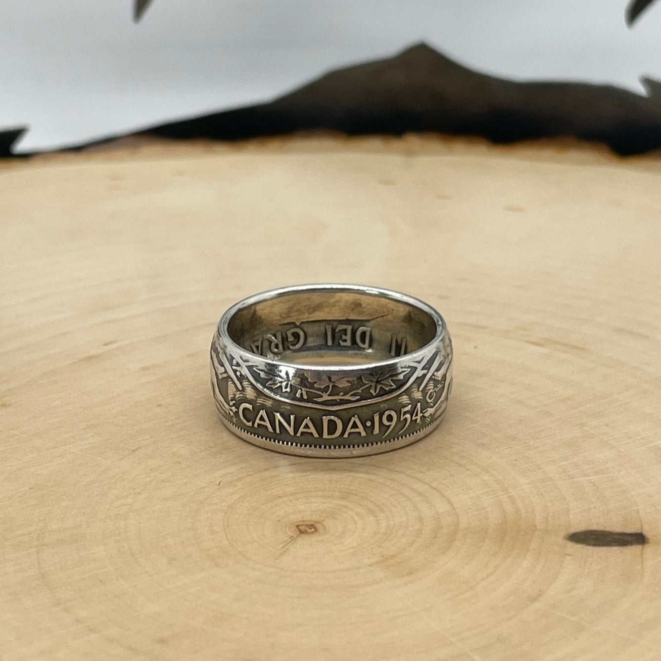 Canada 50 Cents Silver Coin Ring (Lion + Unicorn) on a light wood round with mountain outline in the background. - Mountainstruck Coin Jewelry