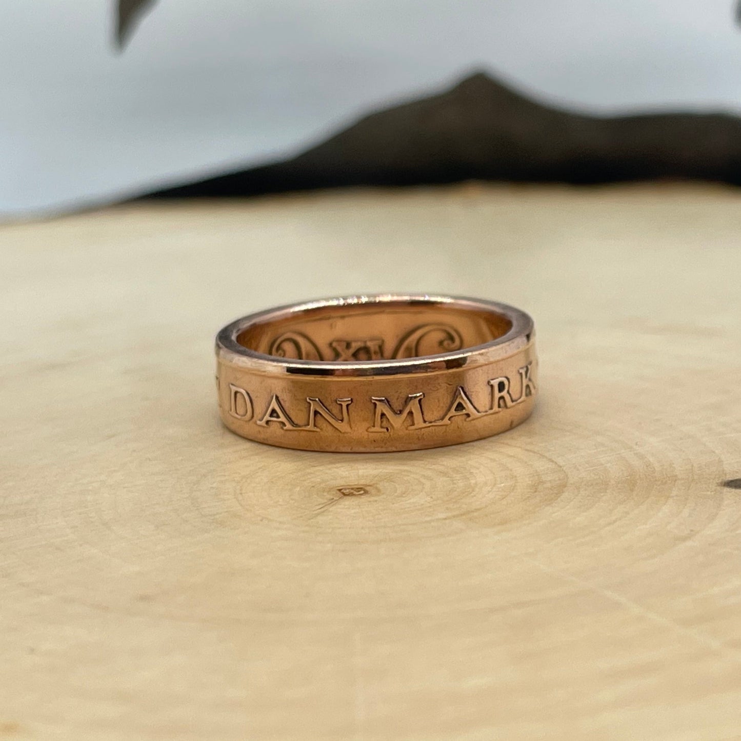 Denmark 5 Øre Coin Ring on a light wood round with a mountain outline background. - Mountainstruck Coin Jewelry