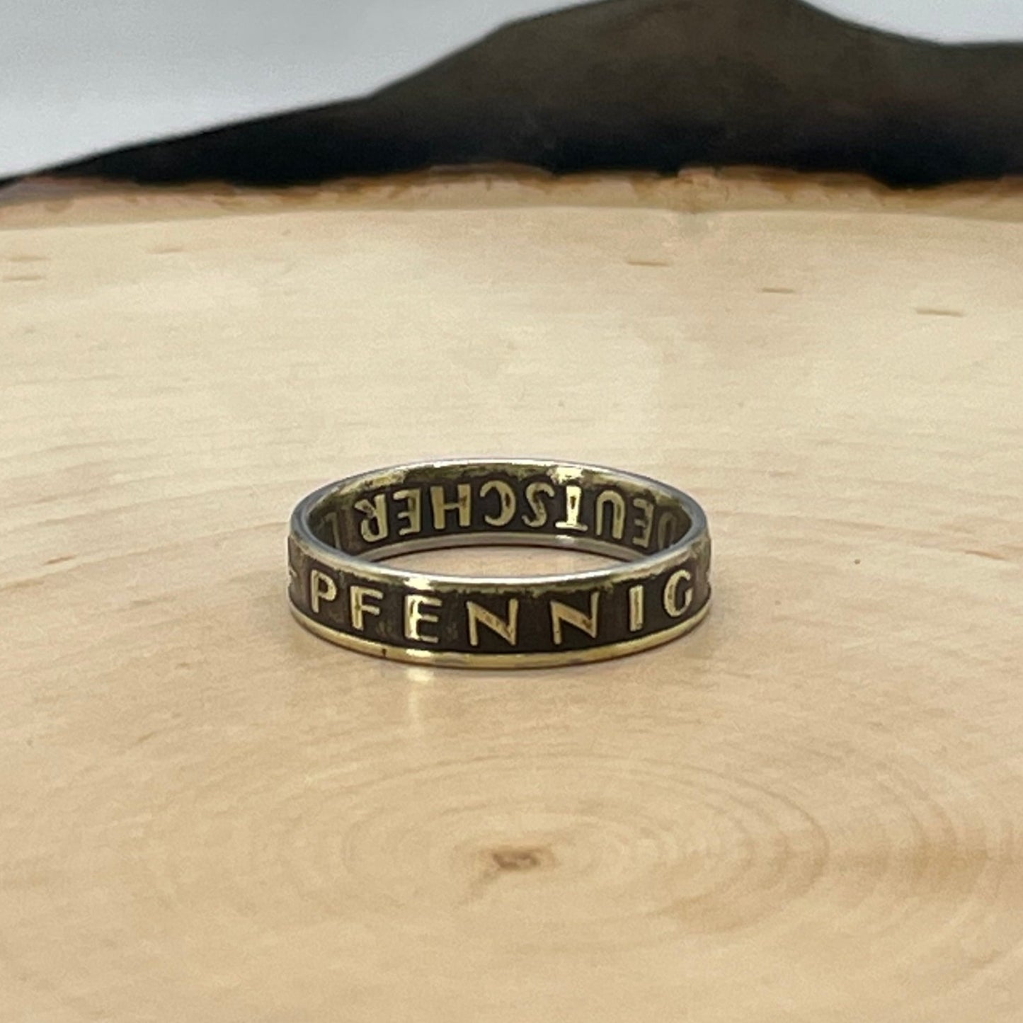 German 5 Pfennig Ring on a light wood round with mountain outline background. - Mountainstruck Coin Jewelry