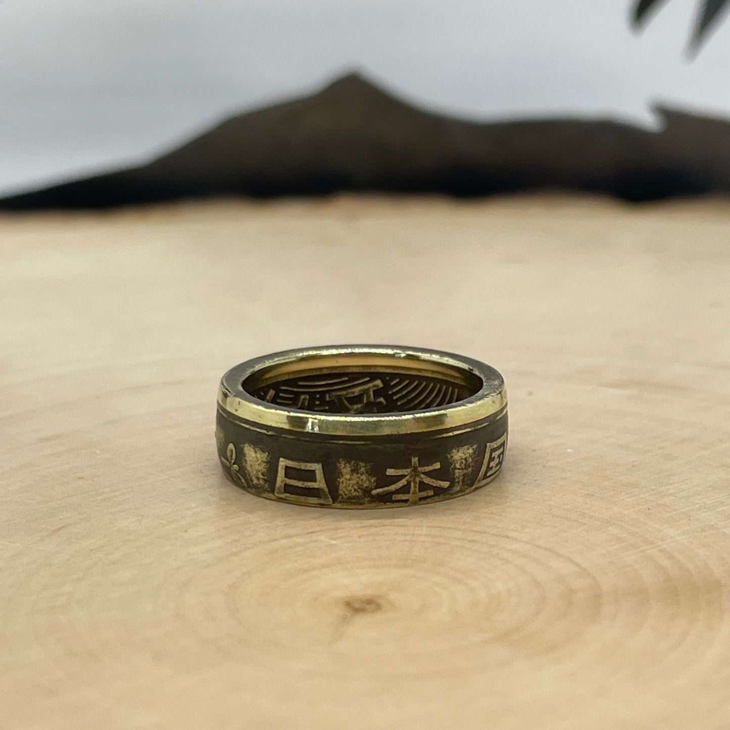 Japan 5 Yen Coin Ring on a light wood round with a mountain outline in the background. - Mountainstruck Coin Jewelry