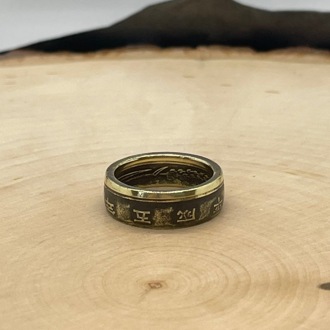 Japan 5 Yen Coin Ring on a light wood round with a mountain outline in the background. - Mountainstruck Coin Jewelry