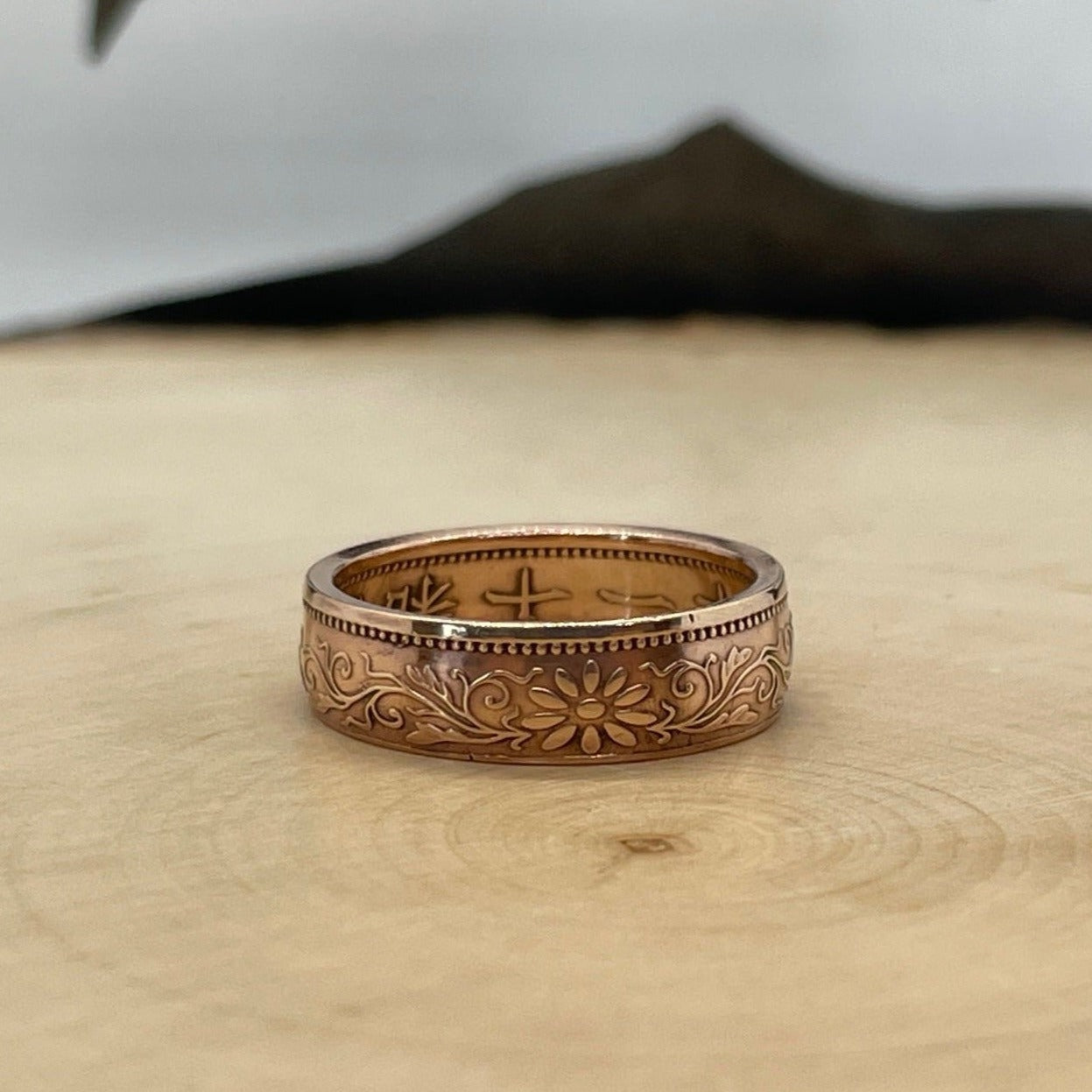 Japan Sen Coin Ring on a light wood round with mountain outline in the background. - Mountainstruck Coin Jewelry