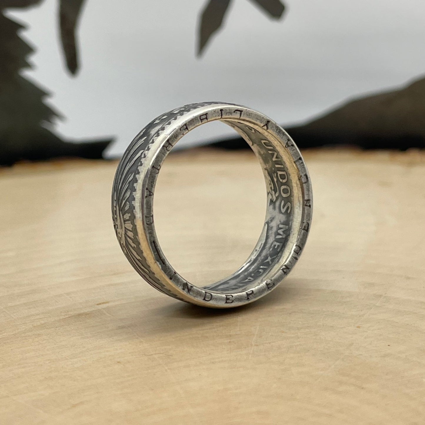 Mexico 50 Centavos Silver Coin Ring (Rare) on its edge on a light wood round with mountain outline in the background. - Mountainstruck Coin Jewelry