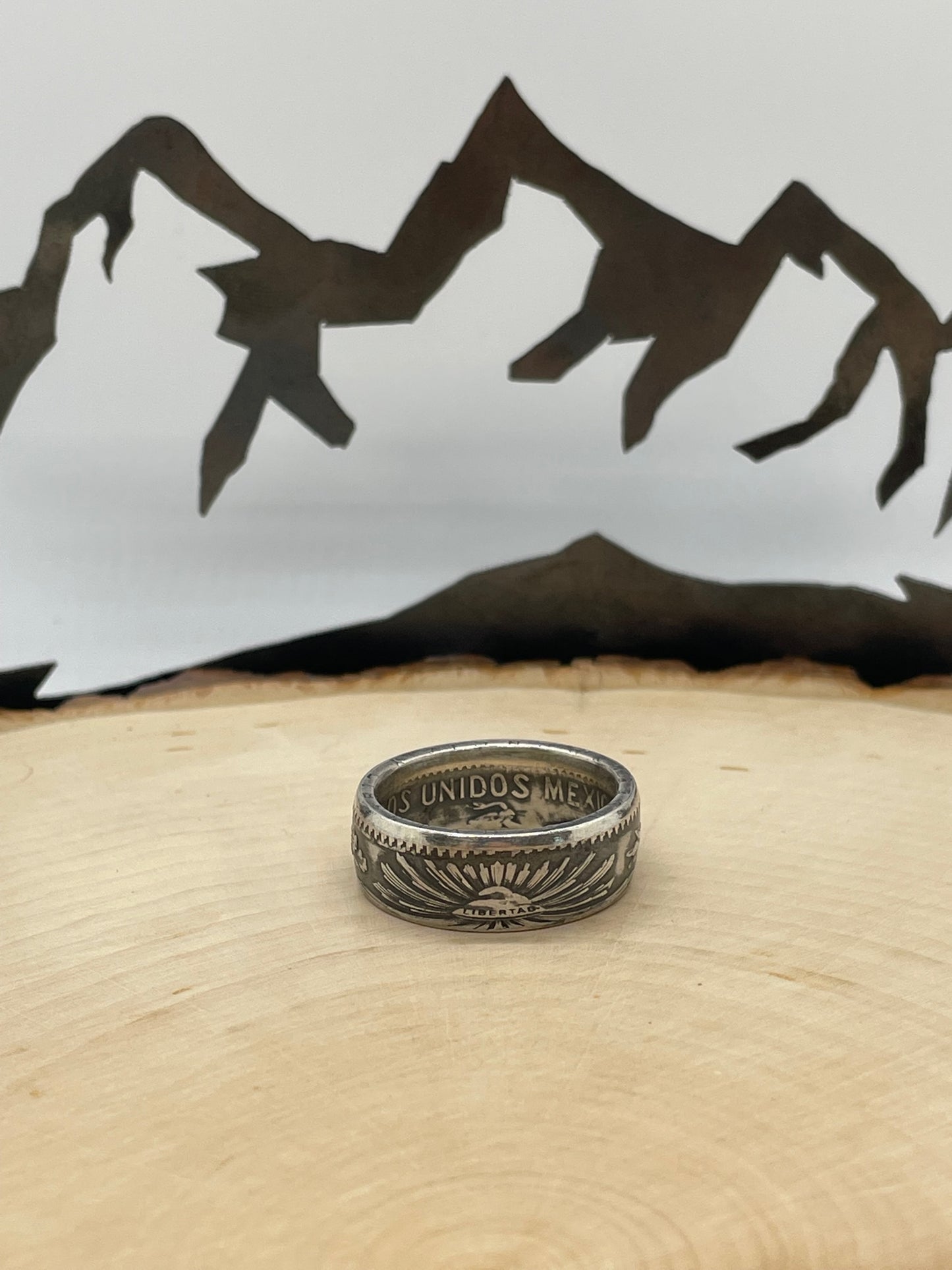 Mexico 50 Centavos Silver Coin Ring (Rare) on a light wood round with mountain outline in the background. - Mountainstruck Coin Jewelry