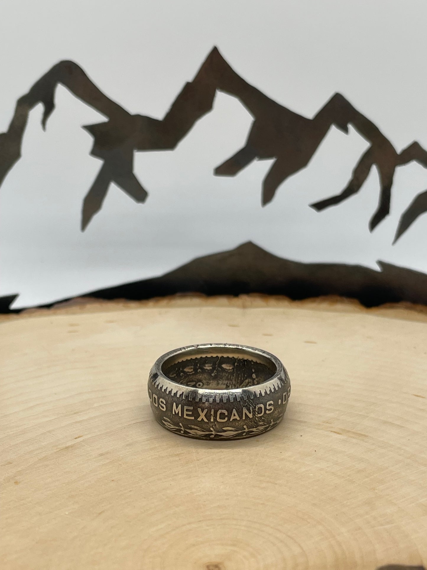 Mexico Silver Peso Coin Ring on a light wood round with mountain outline in the background. - Mountainstruck Coin Jewelry
