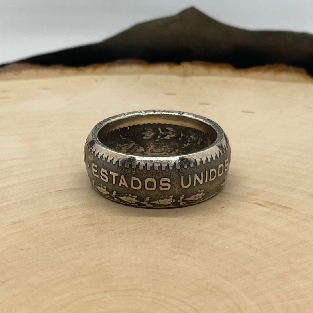 Mexico Silver Peso Coin Ring on a light wood round with mountain outline in the background. - Mountainstruck Coin Jewelry