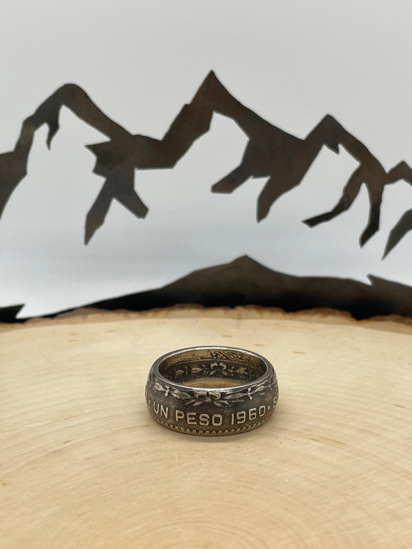 Mexico Silver Peso Coin Ring on a light wood round with mountain outline in the background. - Mountainstruck Coin Jewelry