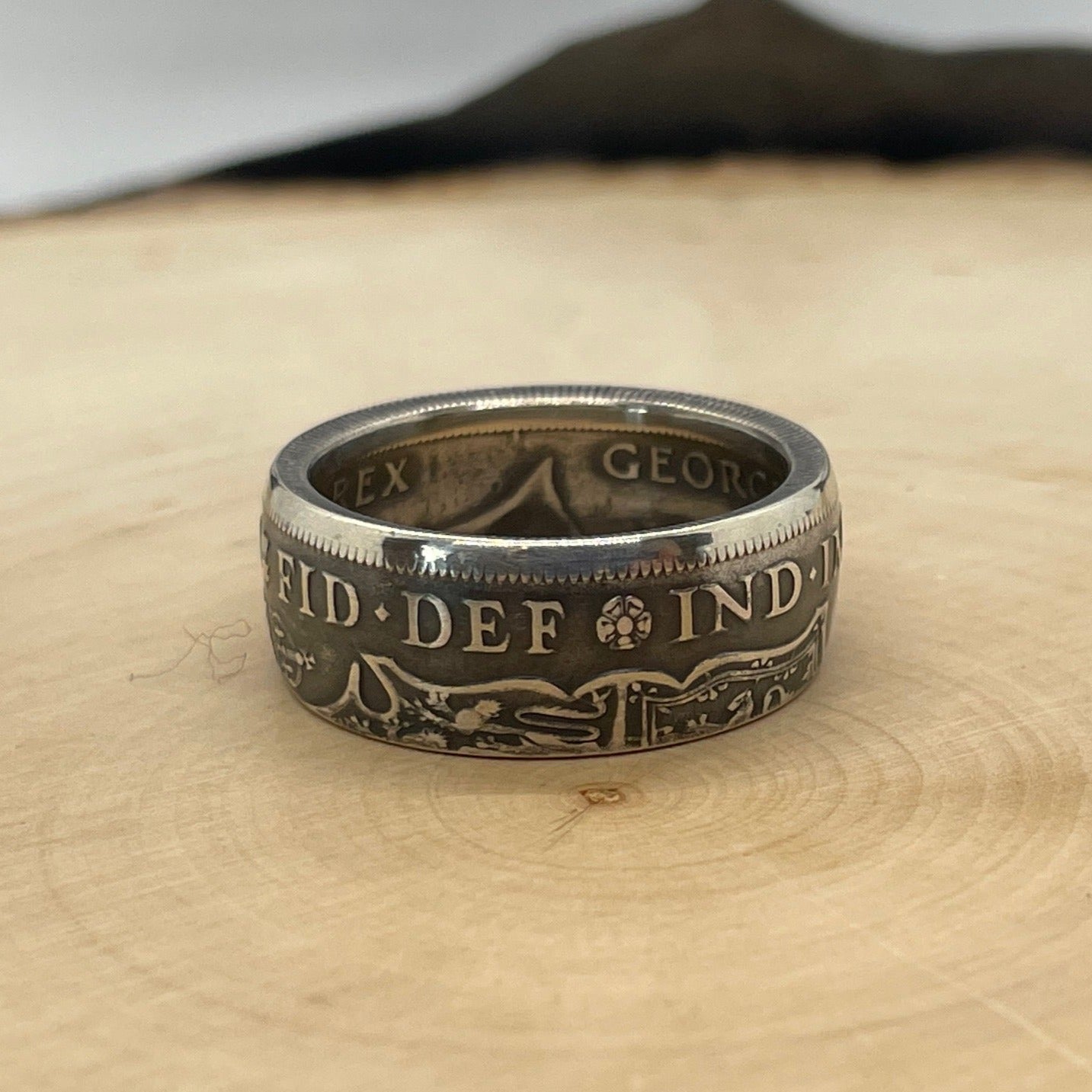UK Half Crown Silver Coin Ring (1927-1936, G.B.) on a light wood round with mountain outline in background. - Mountainstruck Coin Jewelry