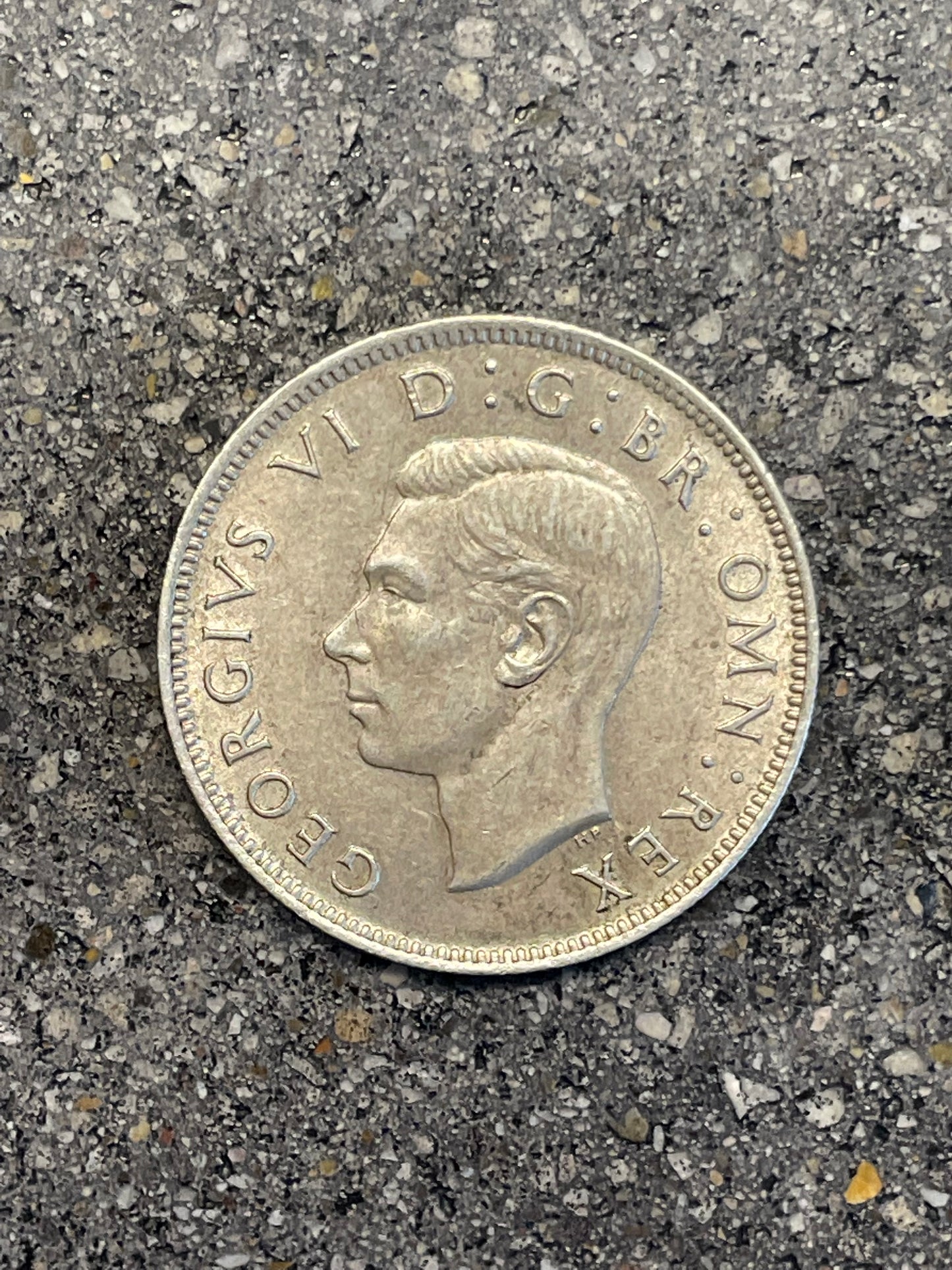 UK Two Shillings Silver Coin front on a concrete background.