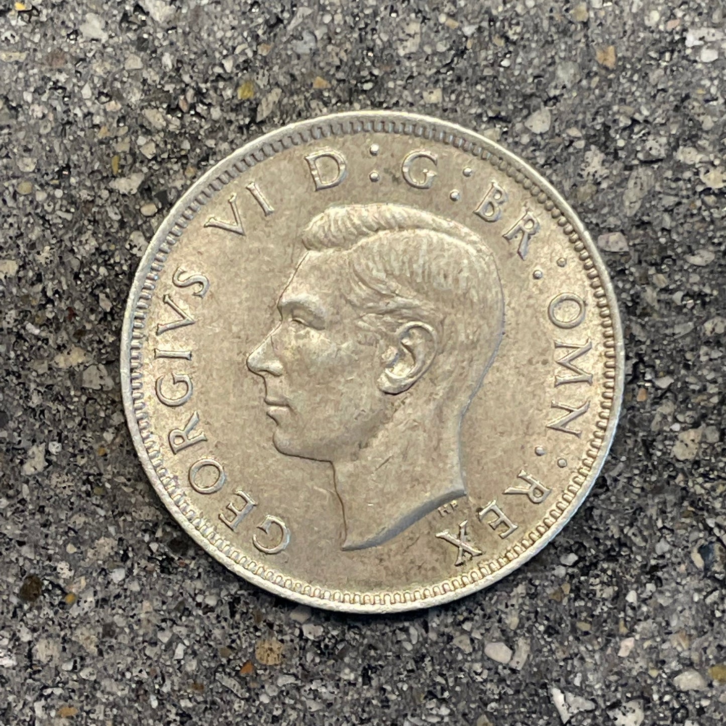 UK Two Shillings Silver Coin front on a concrete background.