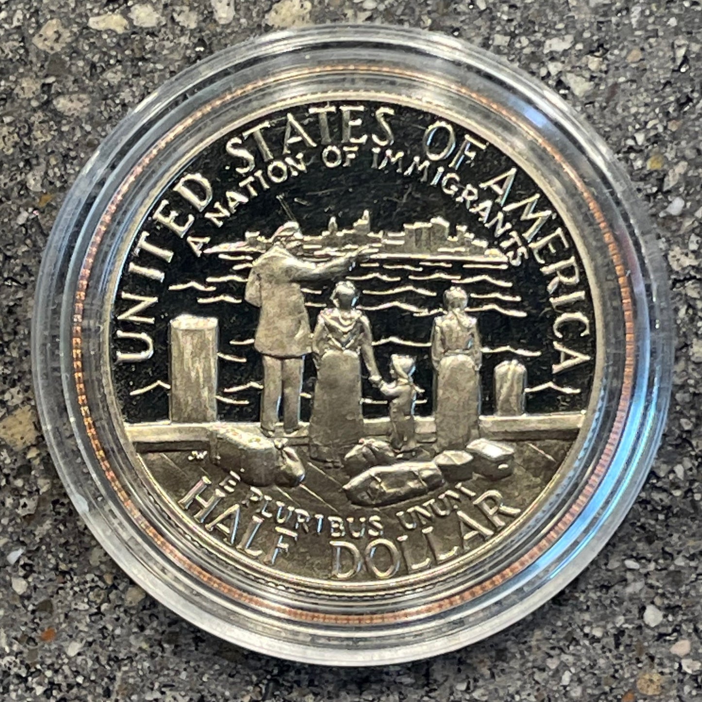 U.S. A Nation of Immigrants Half Dollar back of coin in a plastic case on a concrete background. - Mountainstruck Coin Jewelry