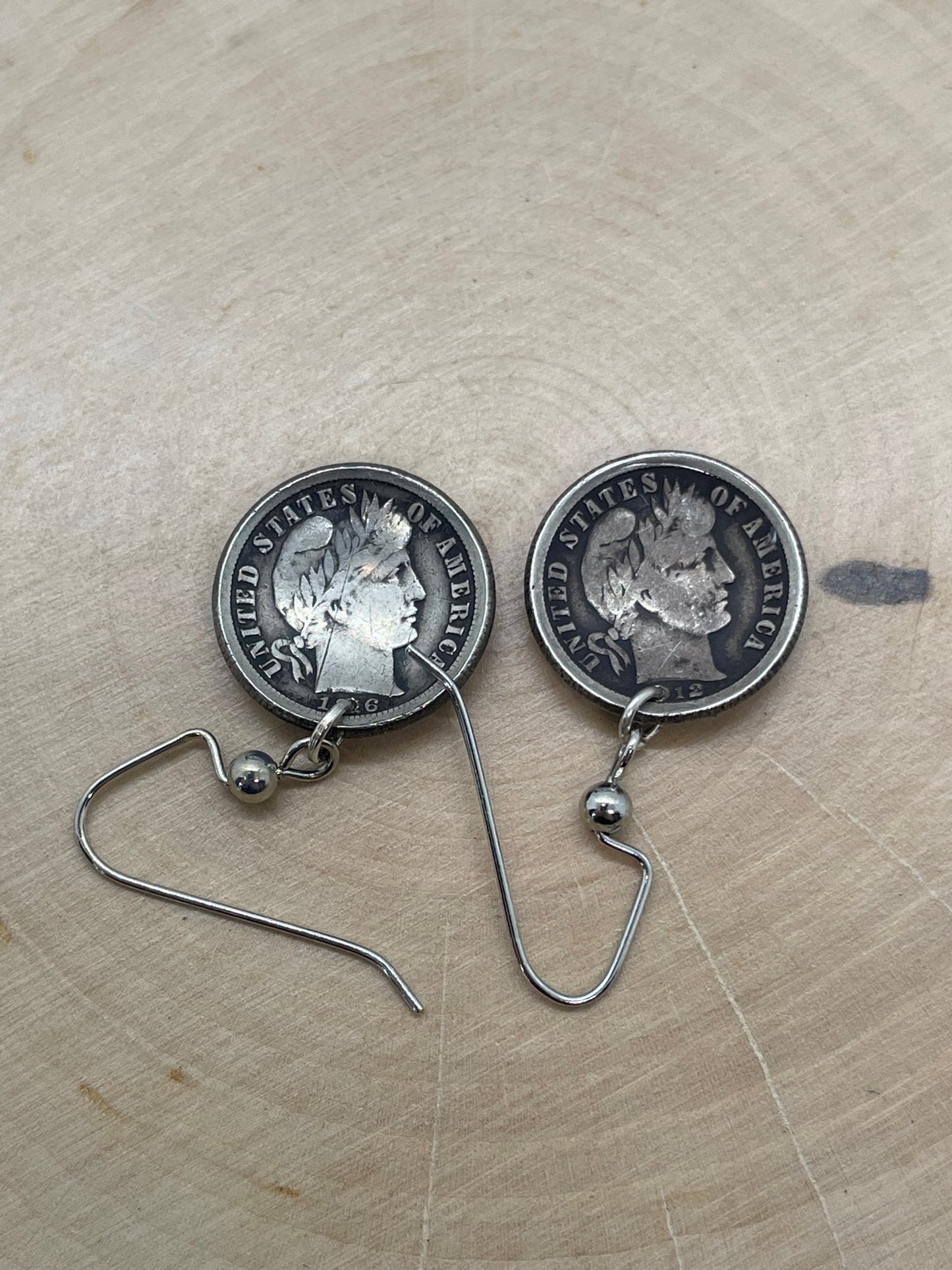 U.S Barber Dime Silver Coin Earring backs on a light wood round.