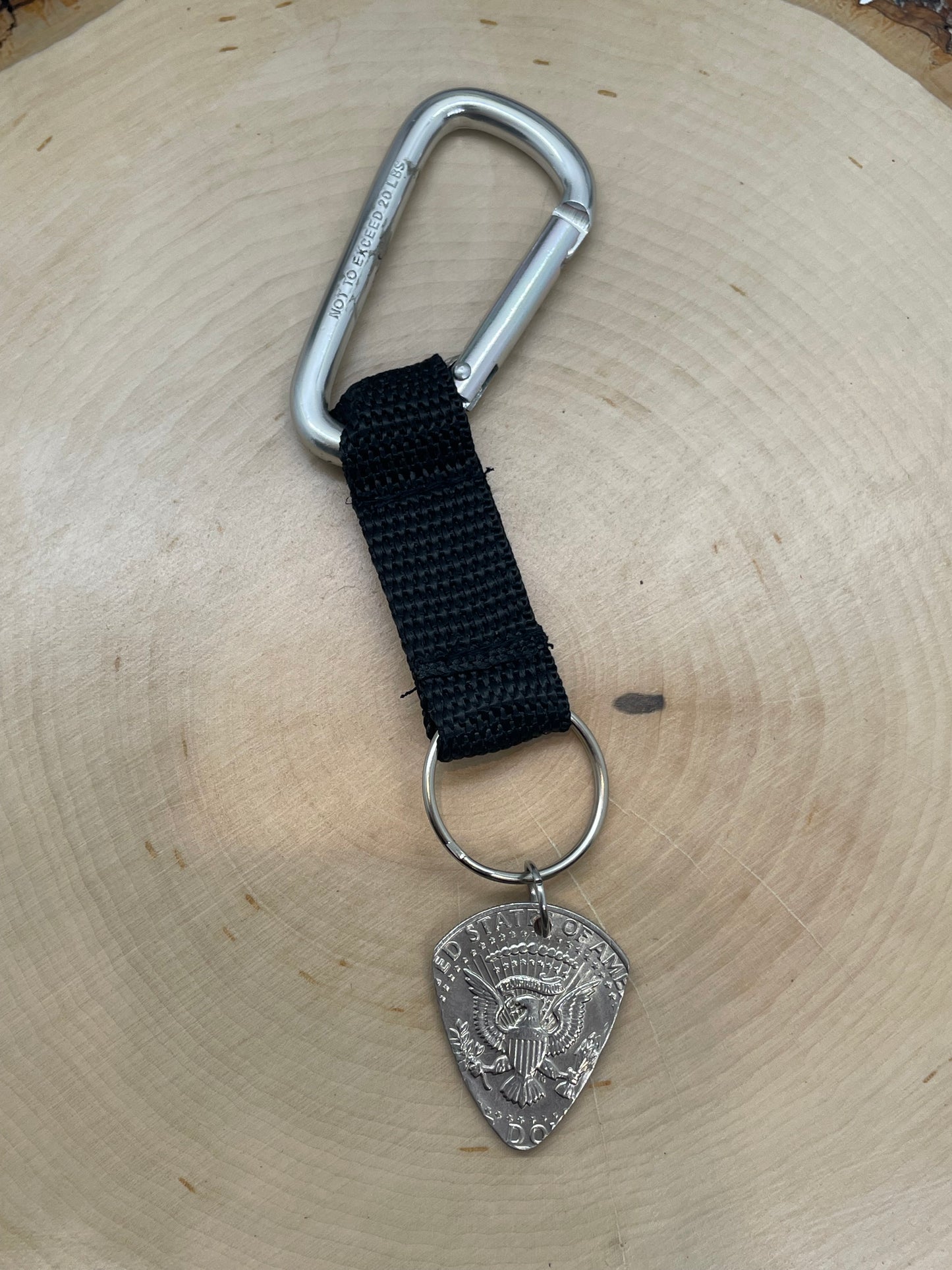 Guitar Pick U.S. Half Dollar Keychain with a black strap on a light wood round.