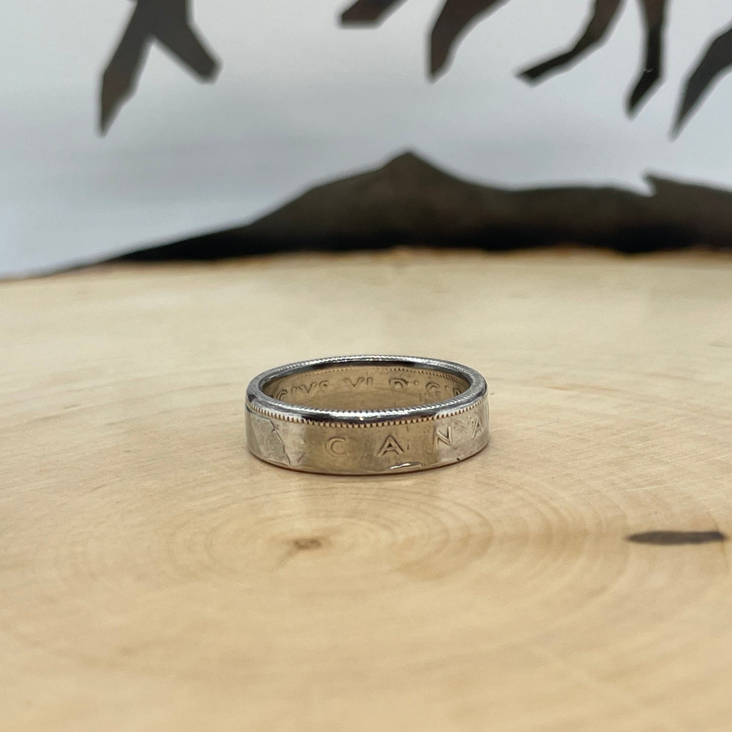 Canada 25 Cents Silver Coin Ring on a light wood round with a mountain outline background.