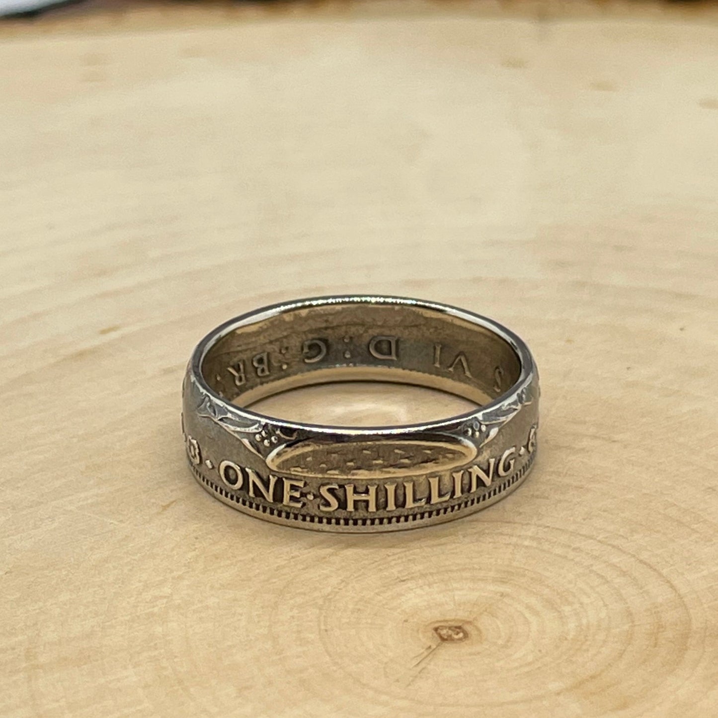 UK One Shilling Silver Coin Ring on a light wood round.