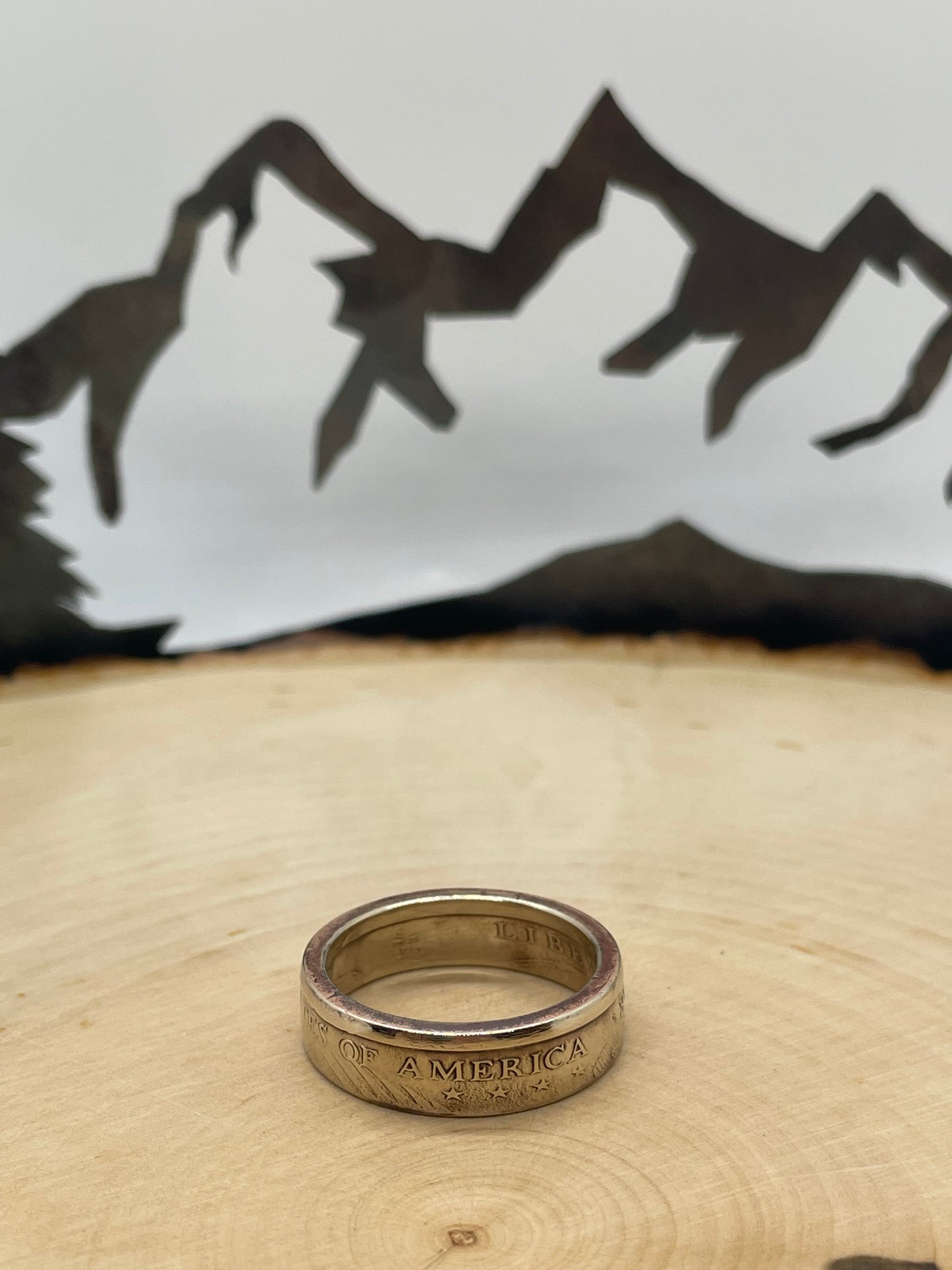 Sacagawea Dollar Coin Ring on a light wood round with mountain outline in background.