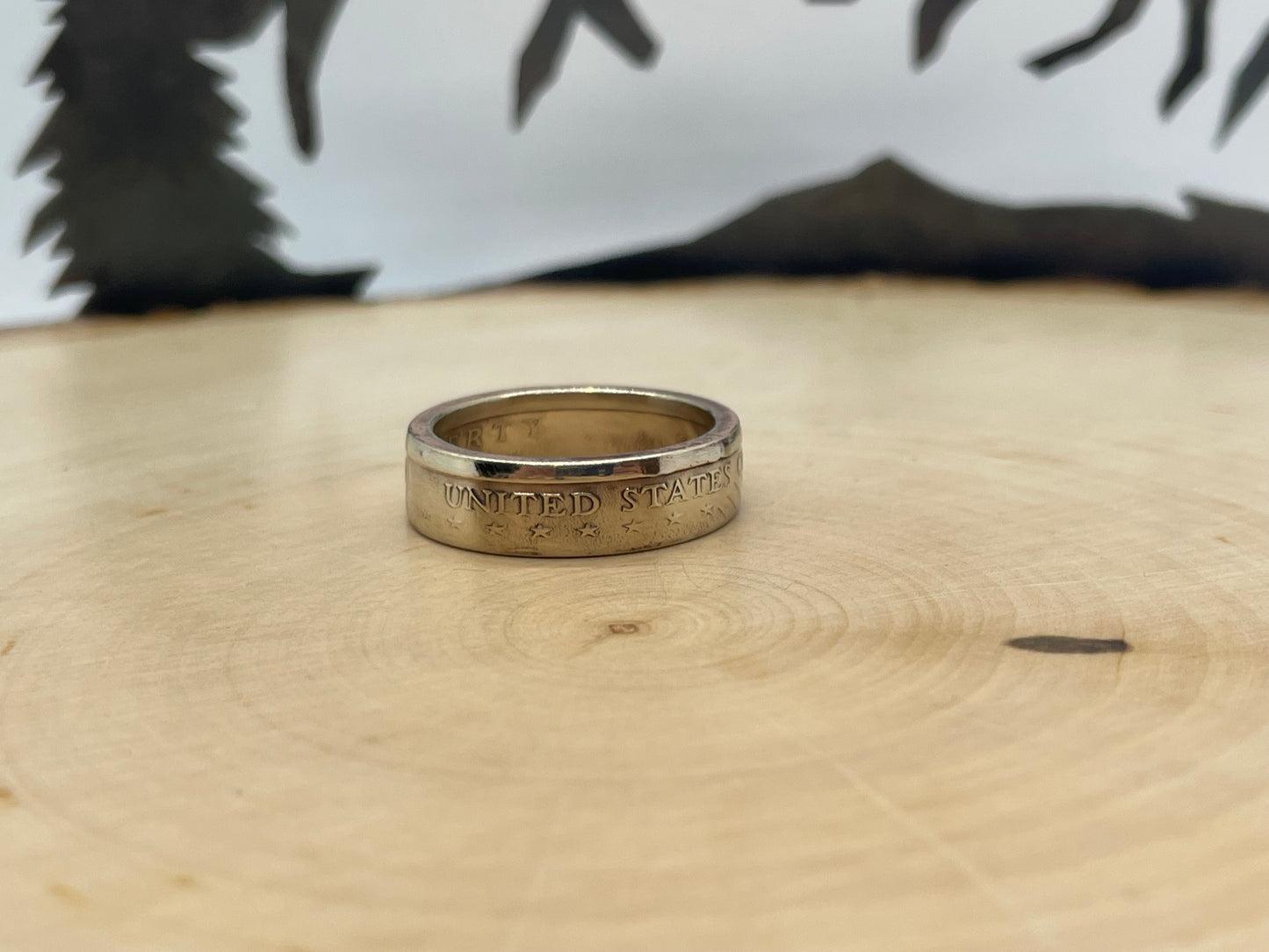 Sacagawea Dollar Coin Ring on a light wood round with mountain outline in background.