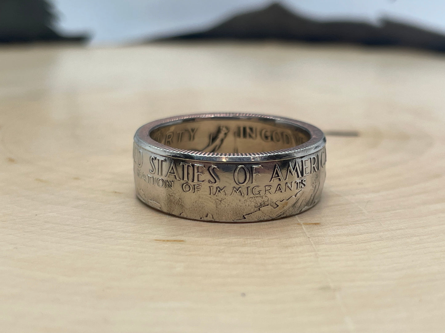 A Nation of Immigrants Half Dollar Coin Ring on wood round.