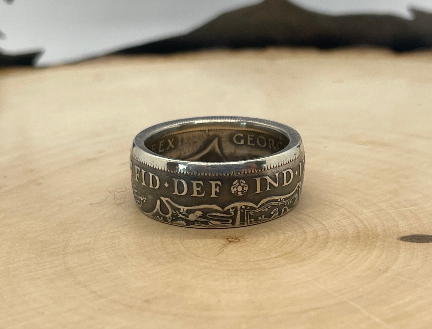 UK Half Crown Silver Coin Ring (1927-1936, G.B.) on a light wood round with mountain outline in background.