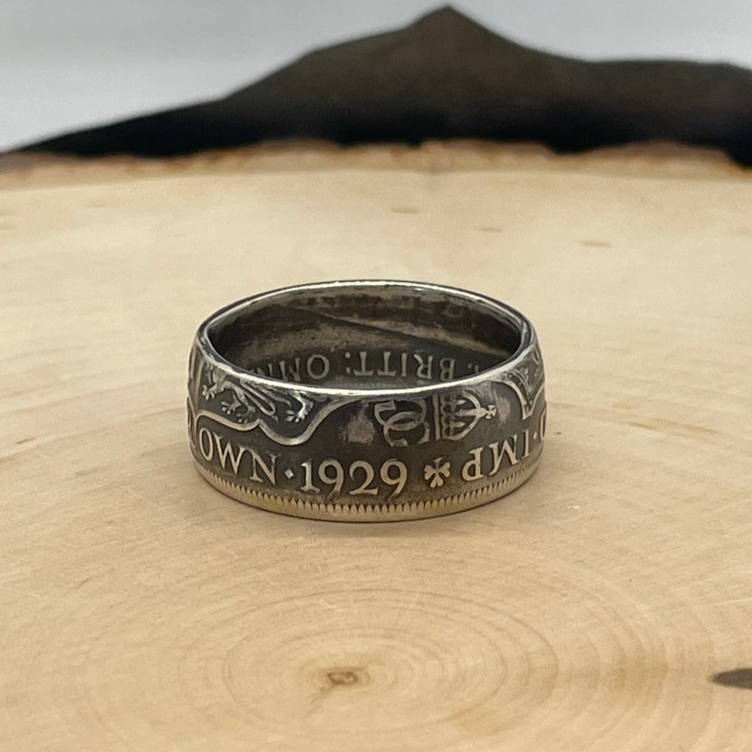 UK Half Crown Silver Coin Ring (1927-1936, G.B.) on a light wood round with mountain outline in background.