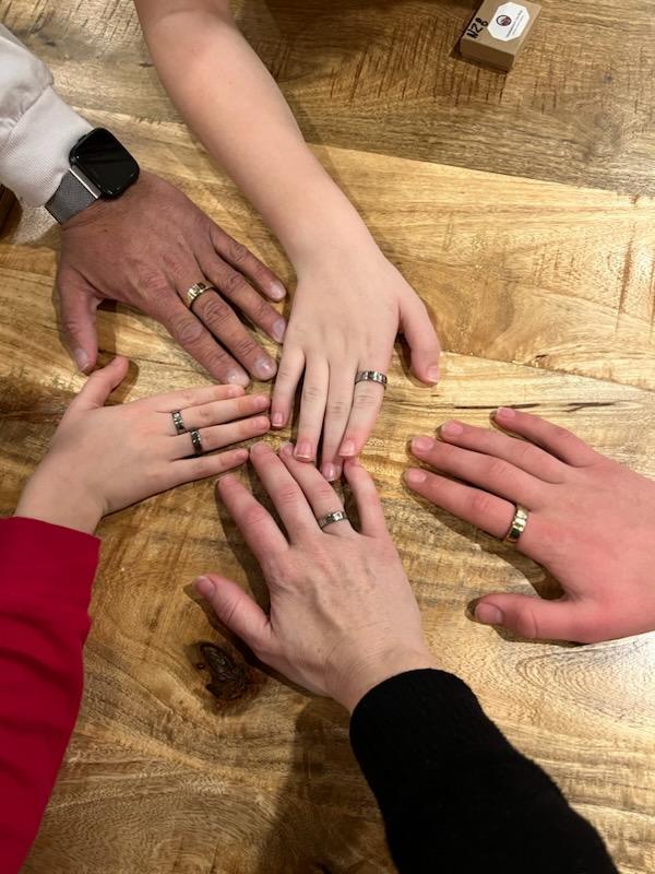 Five hands with varied skin tones showcasing their new family set of New Zealand coin rings on a wood background.