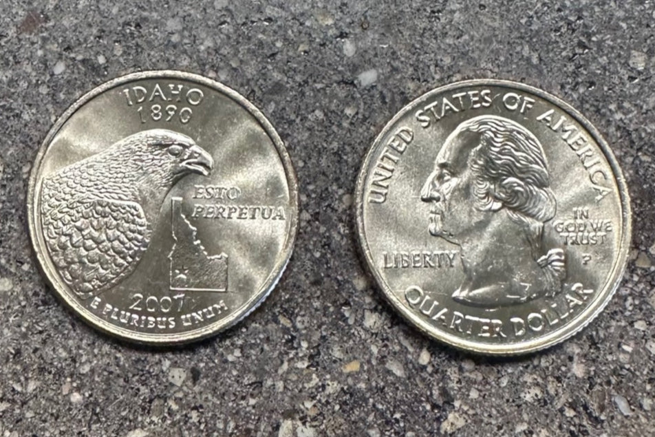 Idaho Quarter Coin on a concrete background. Back side of coin on left of image and front of coin on right side.