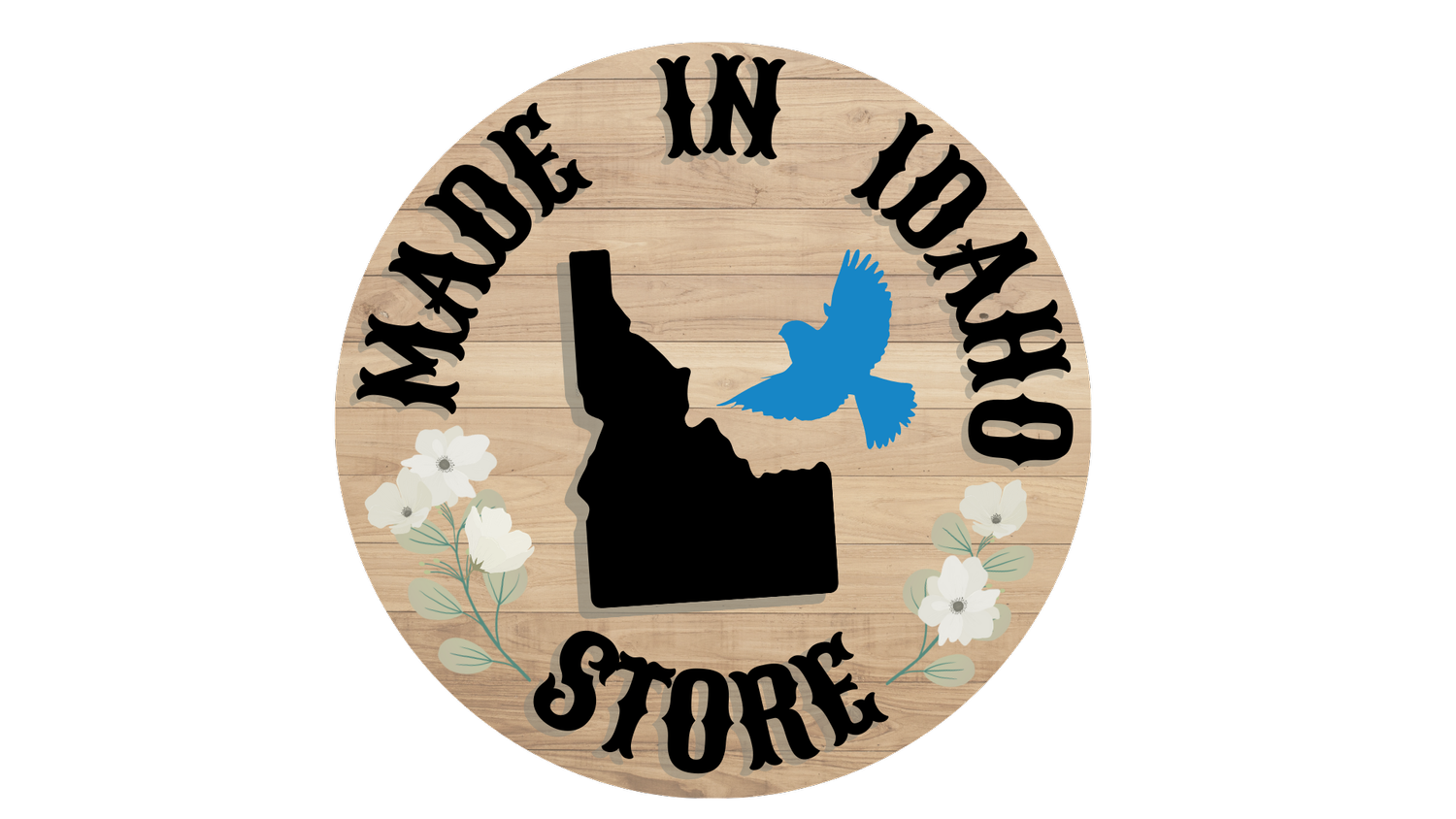 Circular wood logo with bold black text "MADE IN IDAHO" around the top edge. In the middle of the circle is a black Idaho state image and blue bird. At the bottom of the circle is "STORE" with white flowers up both sides.