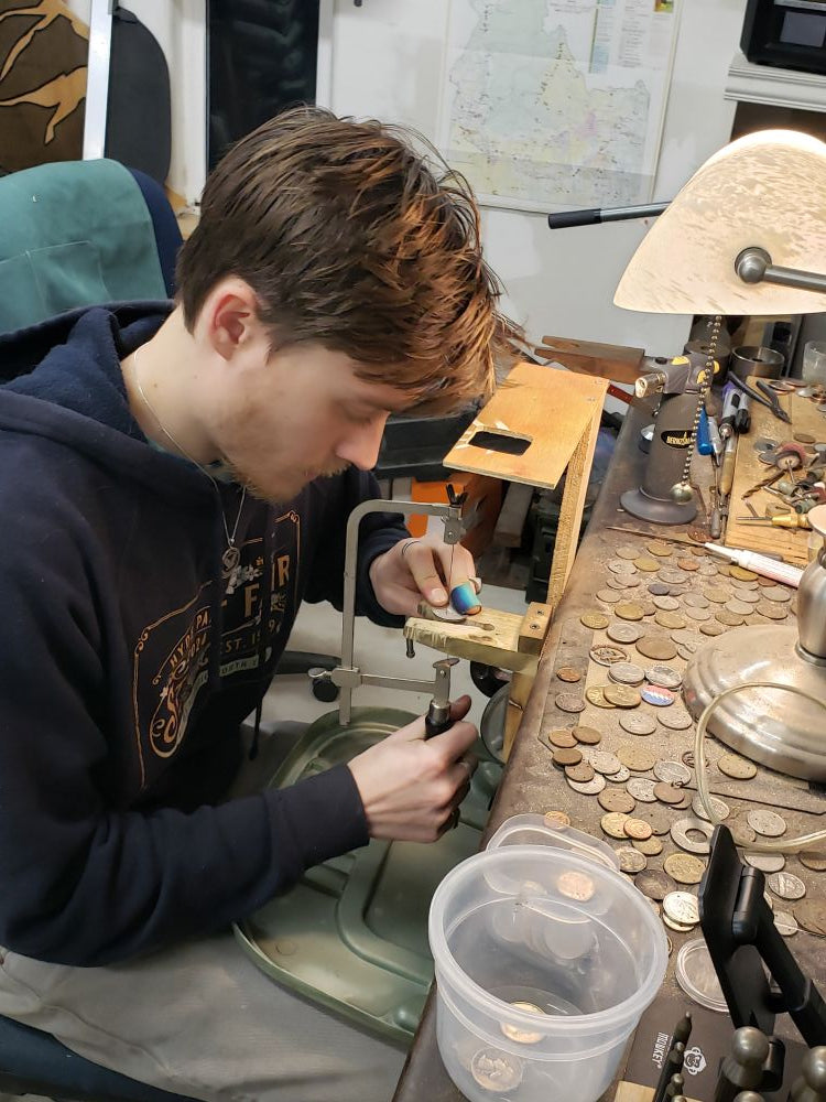 Aidan Poe working on a hand cut coin with his jewelry saw at a workbench in his studio.
-Mountainstruck Coin Jewelry