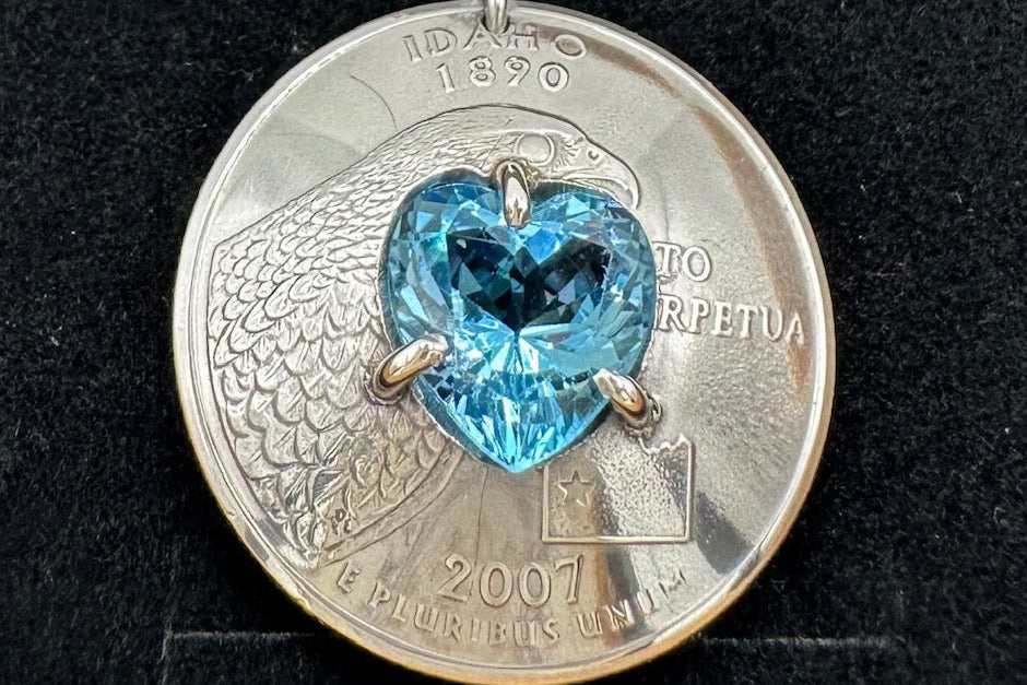 Up close image of rounded Idaho quarter necklace with a heart shaped sky blue topaz soldered into the center. - Mountainstruck Coin Jewelry
