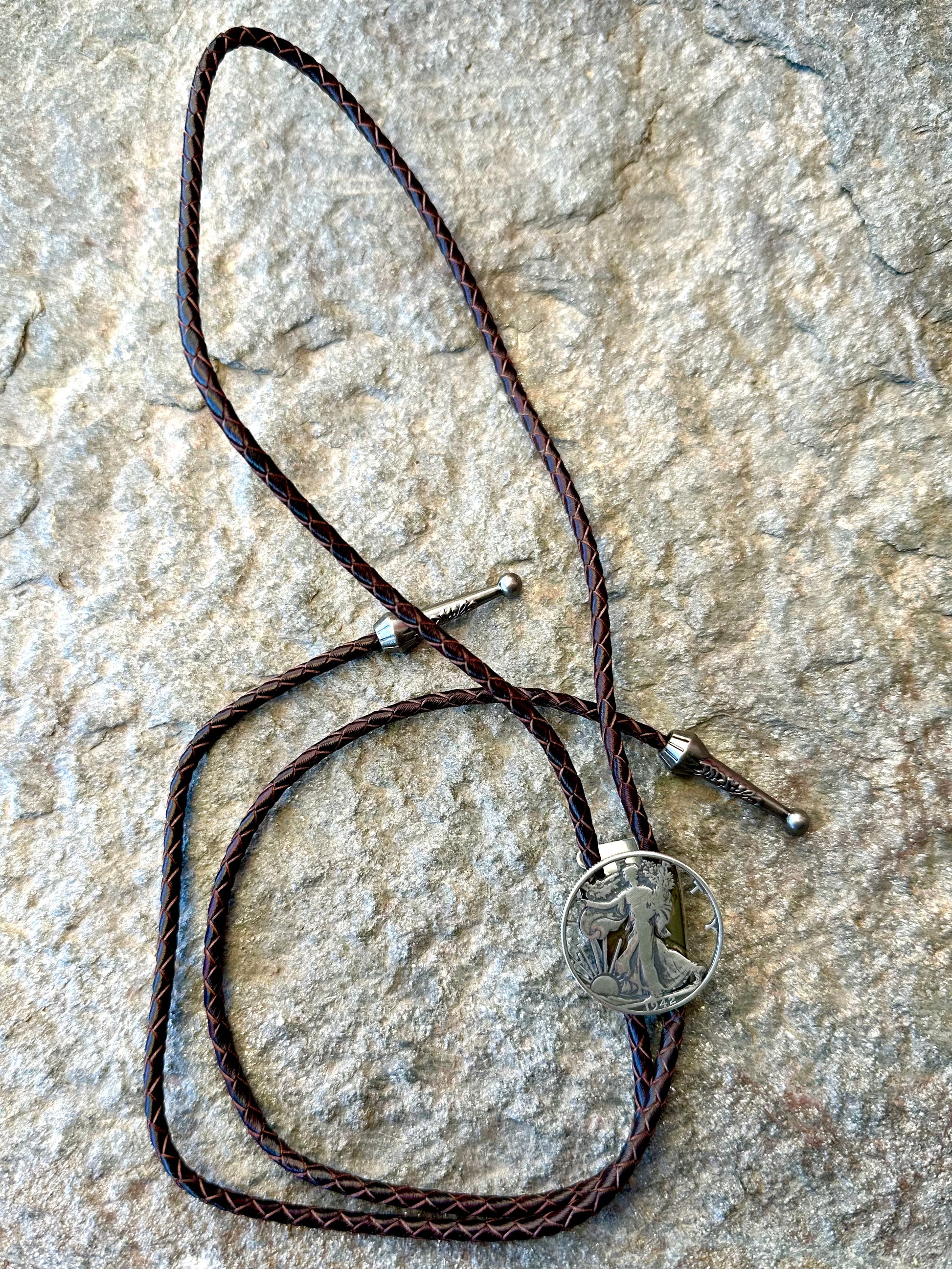U.S. Walking Liberty Half Dollar Hand Cut Silver Coin Bolo Tie on a grey rock surface. - Mountainstruck Coin Jewelry