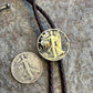 U.S. Walking Liberty Half Dollar Hand Cut Silver Coin Bolo Tie with half dollar coin uncut to the left on a grey rock surface. - Mountainstruck Coin Jewelry