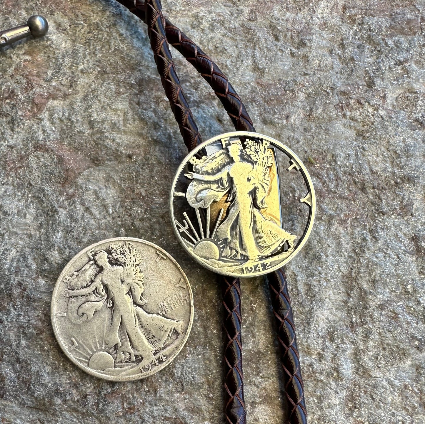 U.S. Walking Liberty Half Dollar Hand Cut Silver Coin Bolo Tie with half dollar coin uncut to the left on a grey rock surface. - Mountainstruck Coin Jewelry