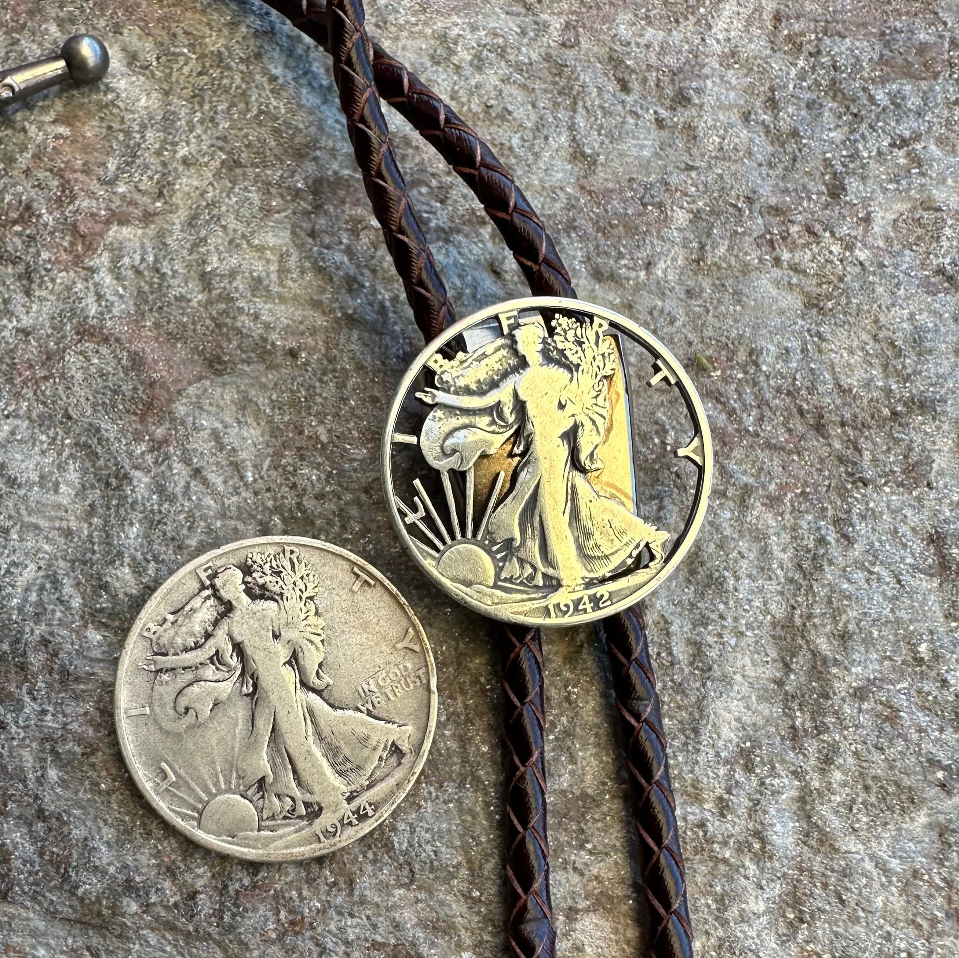 U.S. Walking Liberty Half Dollar Hand Cut Silver Coin Bolo Tie with half dollar coin uncut to the left on a grey rock surface. - Mountainstruck Coin Jewelry