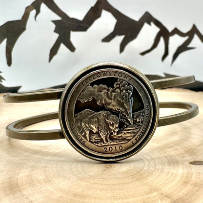 U.S. National Park Quarter Hand Cut Coin Bronze Bracelet on a light wood round with a metal mountain background. - Mountainstruck Coin Jewelry