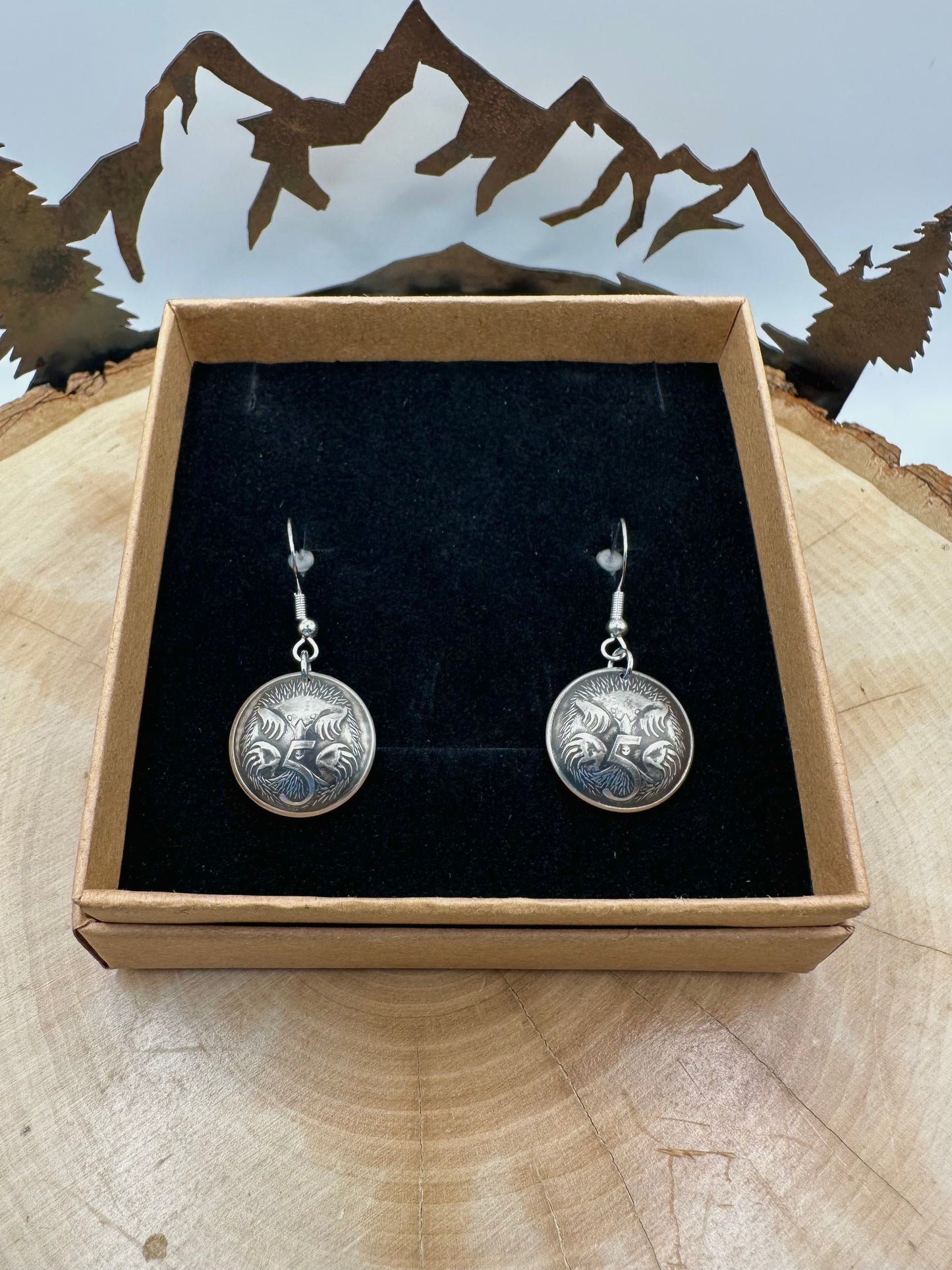 Australia Echidna 5 Cent Domed Coin Earrings in a brown kraft box on a black velvet background on top of a wood round with a metal mountain and tree display. - Mountainstruck Coin Jewelry