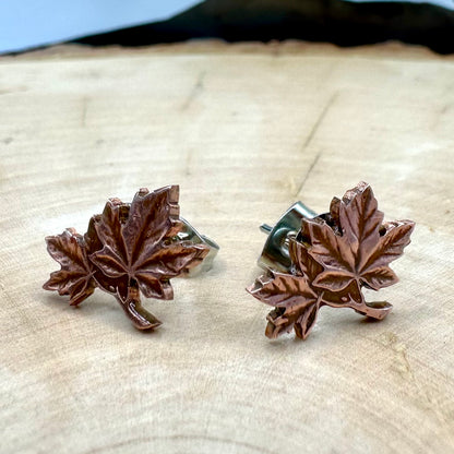 Canada Maple Leaf Penny Stud Coin Earrings on a light wood round metal mountain background. 
- Mountainstruck Coin Jewelry