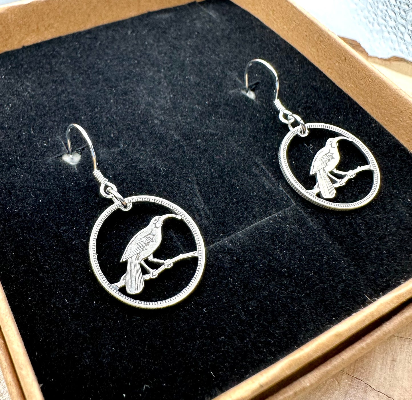 New Zealand Huia Bird 6 Pence Silver Hand Cut Coin Earrings in a brown kraft box on a black velvet background. - Mountainstruck Coin Jewelry