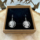 U.S. Buffalo Nickel Hand Cut Coin Earrings (Front) in a brown kraft box on black velvet background on top of a light wood round with a metal mountain and tree display. - Mountainstruck Coin Jewelry