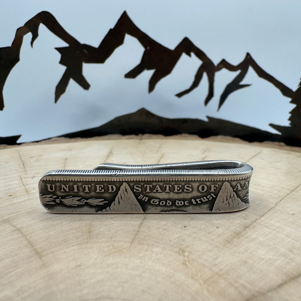 U.S. Morgan Dollar Silver Coin Money Clip on a light wood round with a hand cut metal mountain background.
- Mountainstruck Coin Jewelry