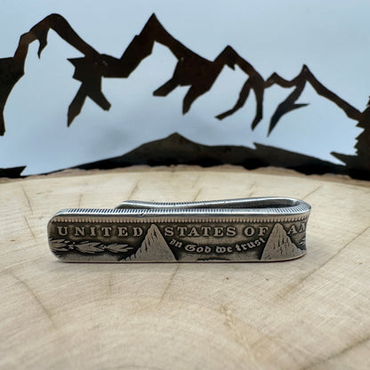 U.S. Morgan Dollar Silver Coin Money Clip on a light wood round with a hand cut metal mountain background.
- Mountainstruck Coin Jewelry