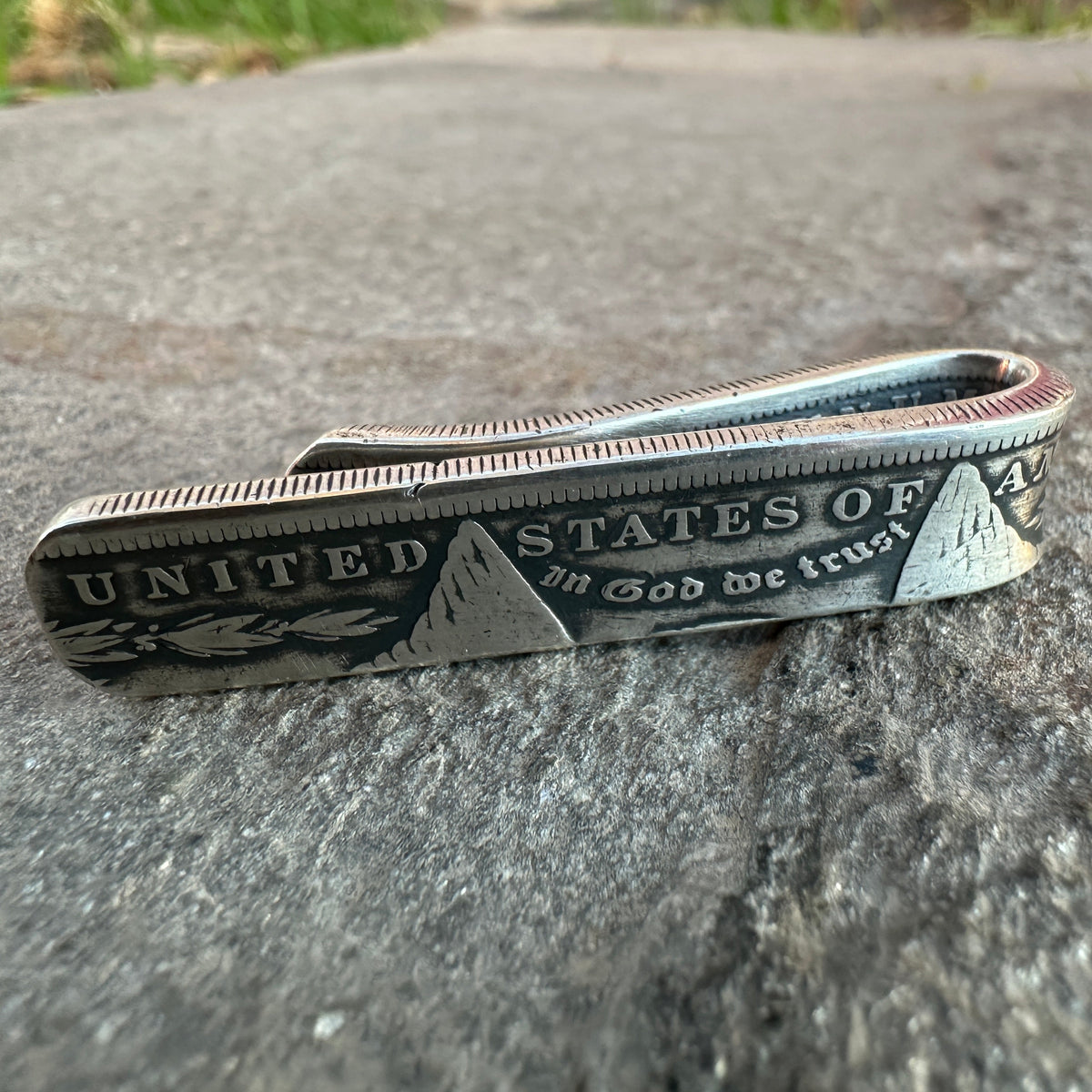U.S. Morgan Dollar Silver Coin Money Clip on a textured rock with grass in the background.
- Mountainstruck Coin Jewelry