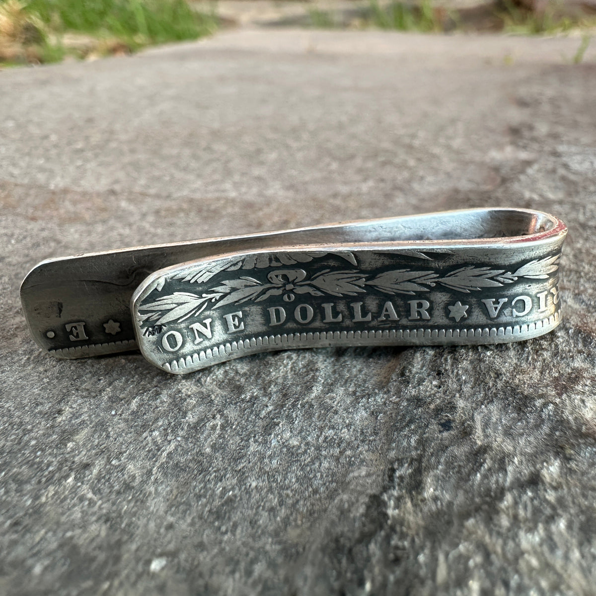 U.S. Morgan Dollar Silver Coin Money Clip on a textured rock with grass in the background.
- Mountainstruck Coin Jewelry